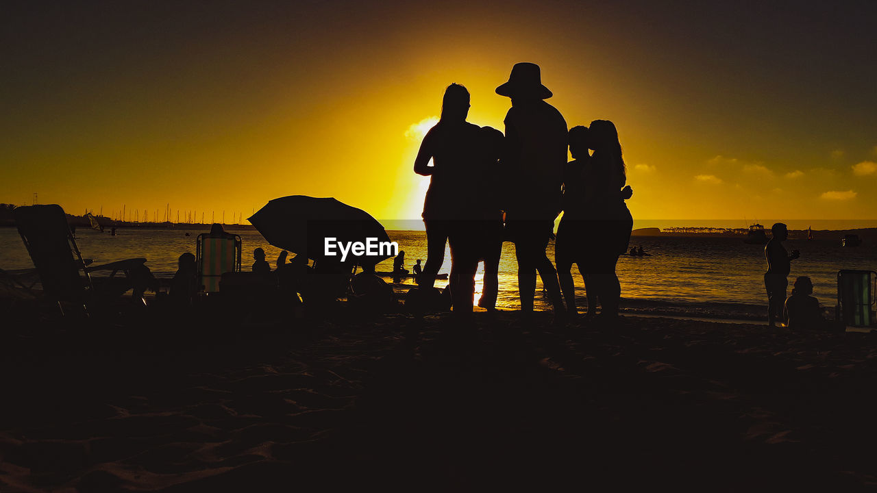 SILHOUETTE PEOPLE STANDING ON BEACH AGAINST SKY DURING SUNSET