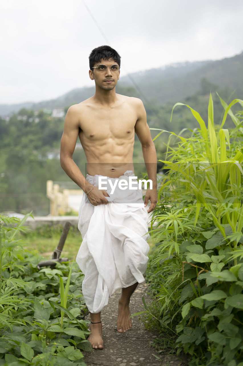 Young indian fit boy, walking on a pathway beside crops in the field. an indian priest walking .