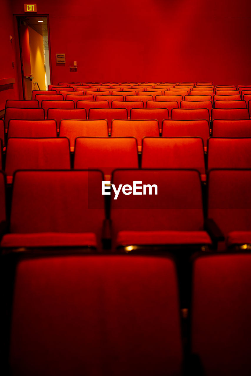 Bright red auditorium with rows of empty red cloth covered seats and open exit door