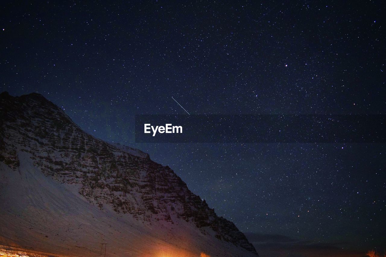 Low angle view of snowcapped mountain against star field sky at night