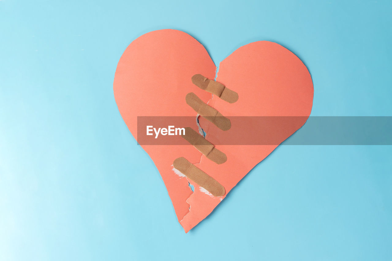 Close-up of heart shape paper with bandage against blue background