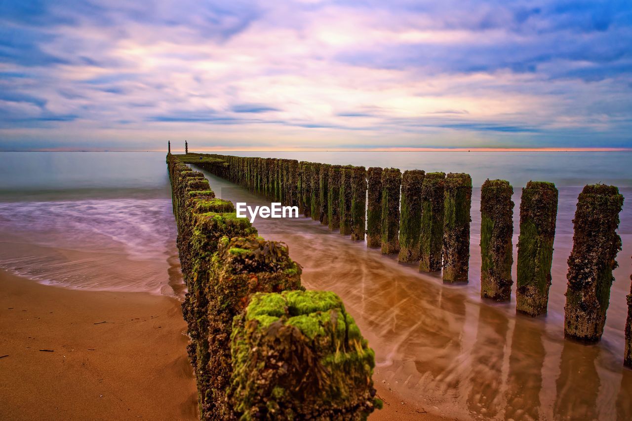 WOODEN POSTS ON BEACH AGAINST SKY