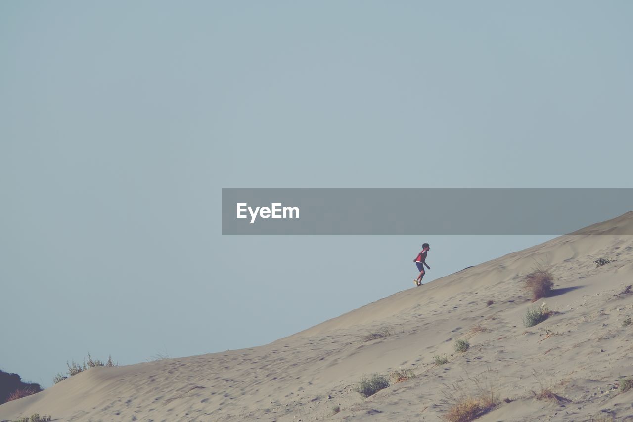 LOW ANGLE VIEW OF PERSON STANDING ON SAND DUNE