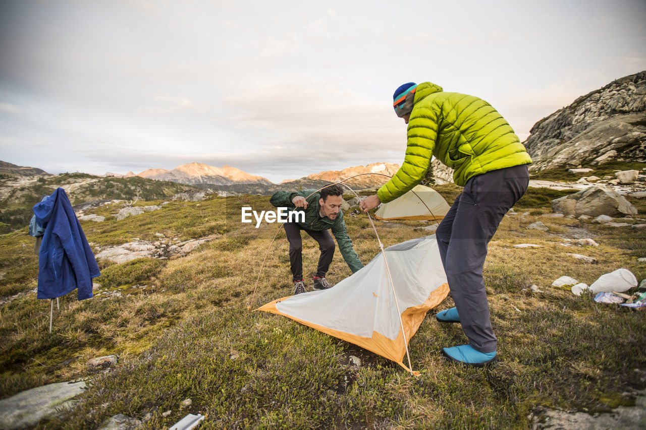 Two backpackers set up tent in alpine meadow.