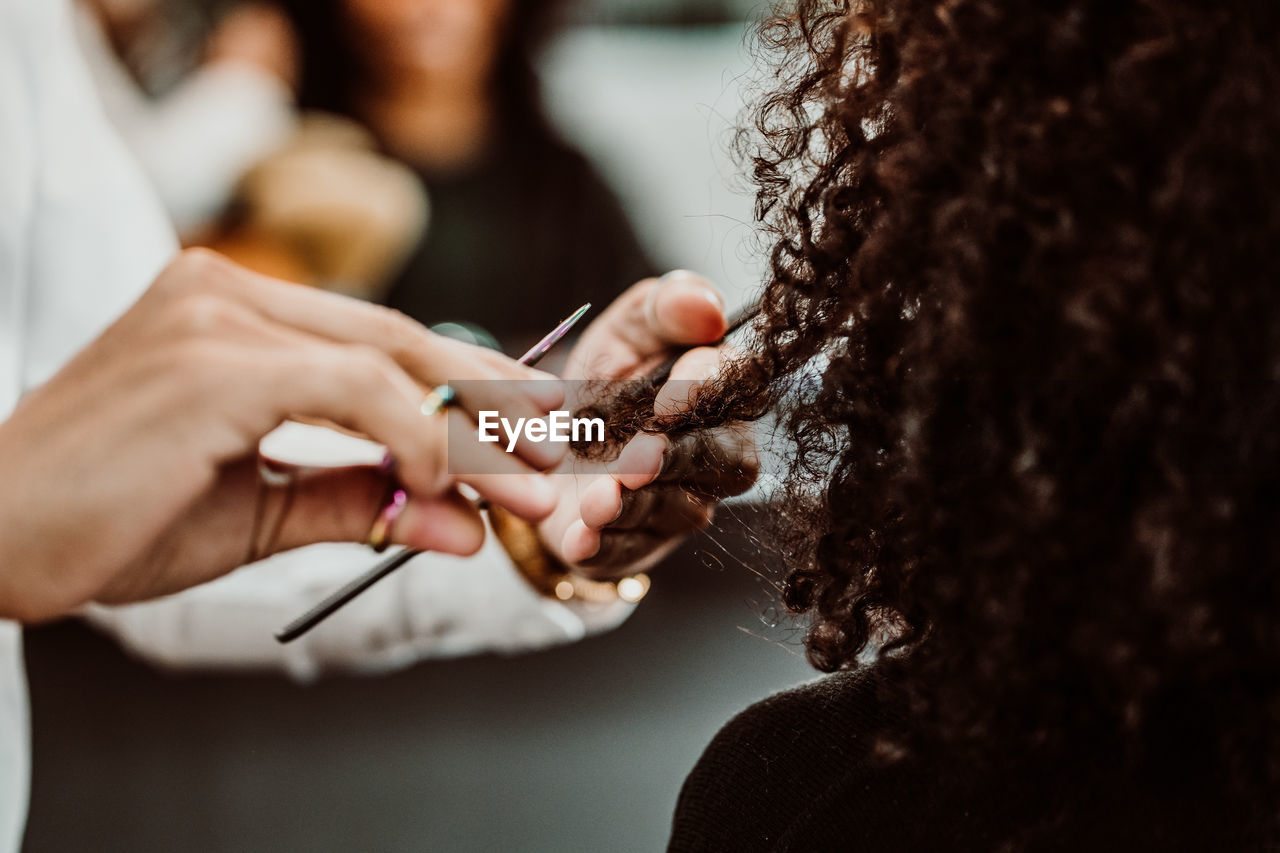 Cropped hands of barber cutting woman hair in salon