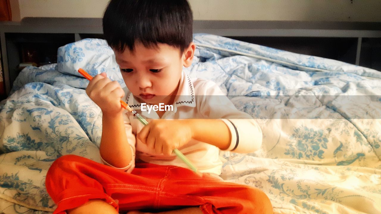 Cute baby boy sitting on bed at home