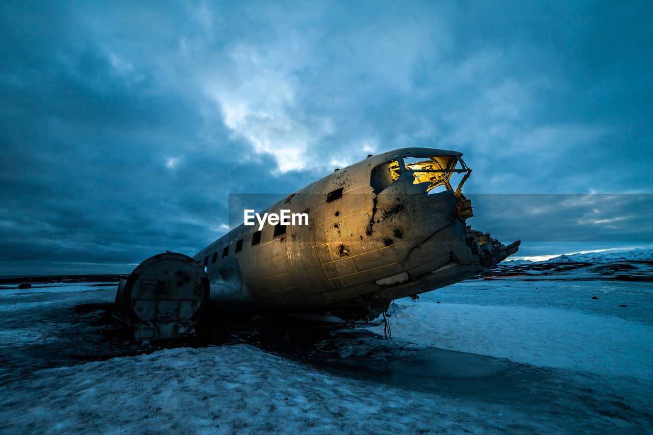 Piece of huge crashed plane in frozen lake against dark cloudy sky in iceland