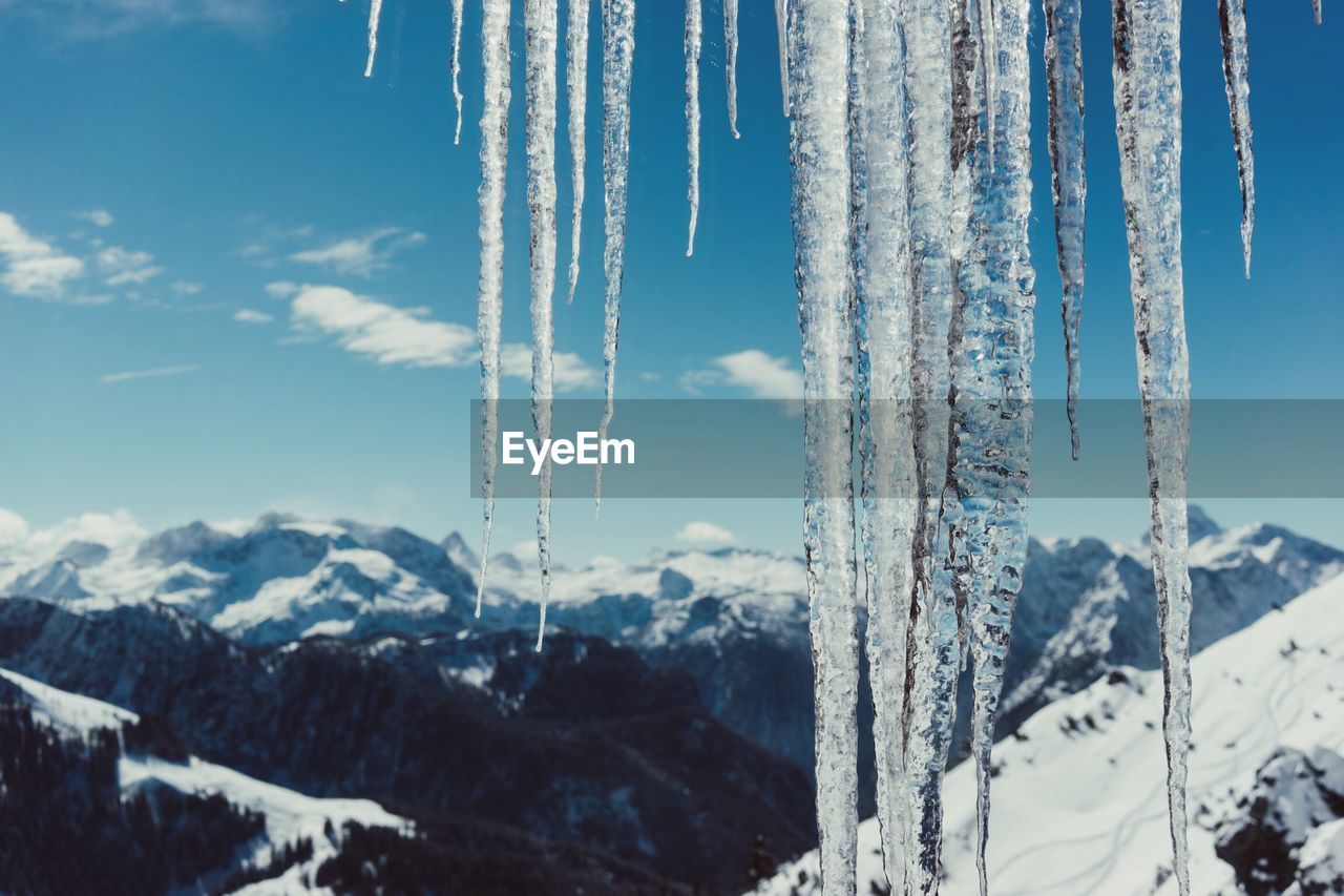 Close-up of icicles by snow covered mountains against sky