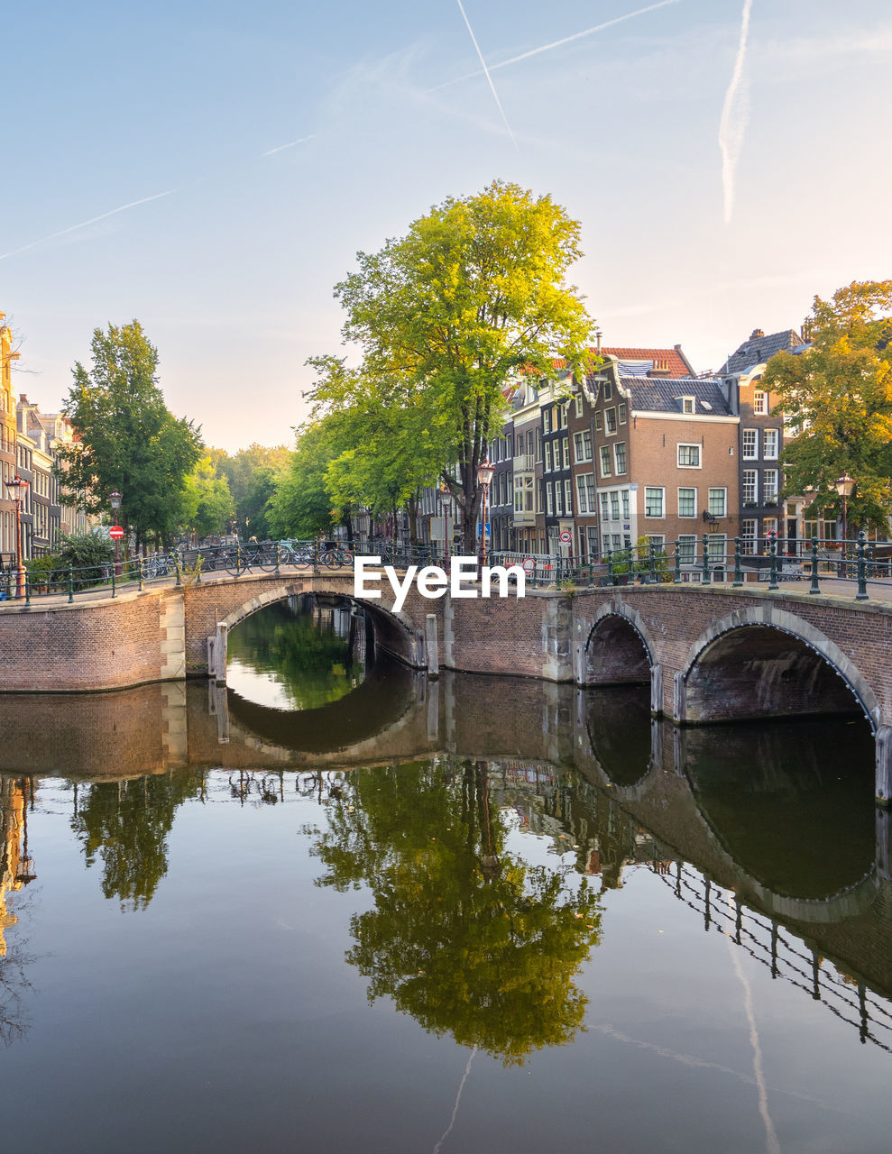 Serene morning scene in amsterdam with traditional houses, bikes on a bridge, and canal reflection.