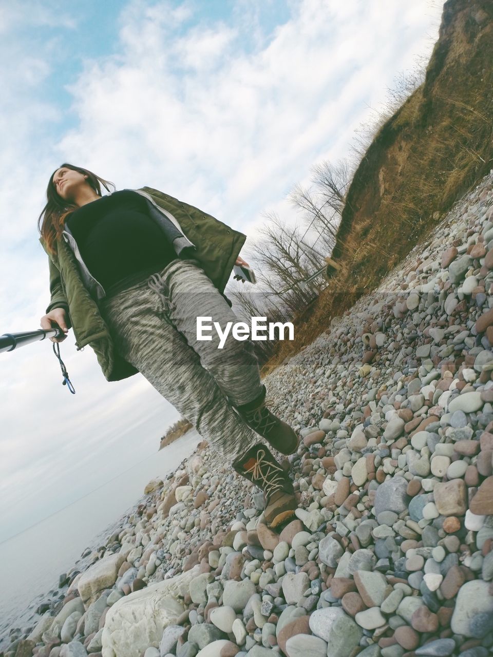 Low angle view of woman with monopod walking on stones against sky