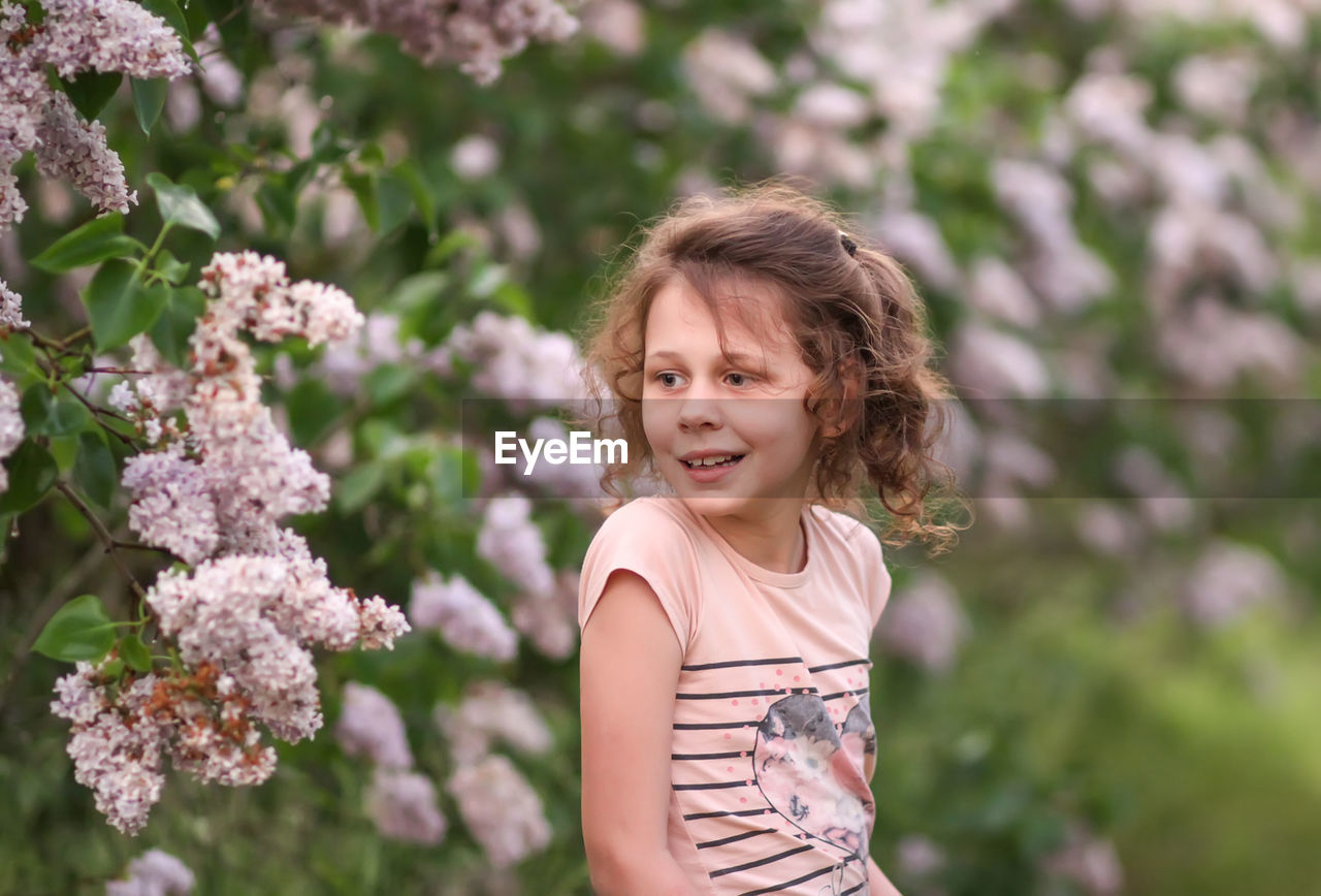 PORTRAIT OF A SMILING GIRL STANDING AGAINST PLANTS OUTDOORS