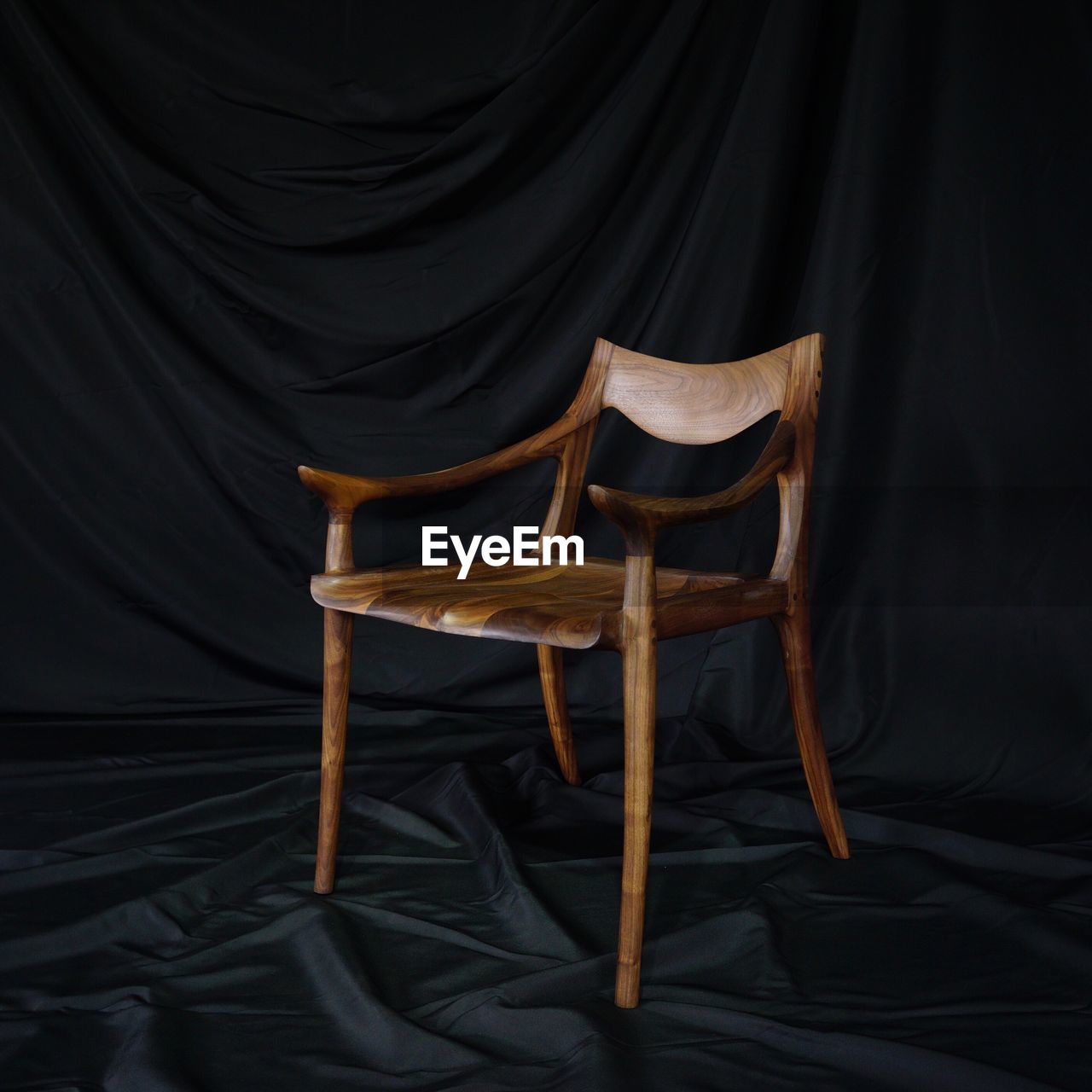 Empty wooden chair against black textile