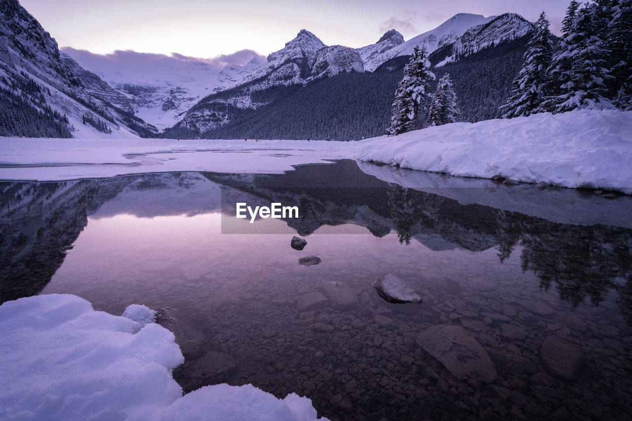 Purple winter sunset on the bank of partially frozen lake, shot at lake louise, alberta, canada