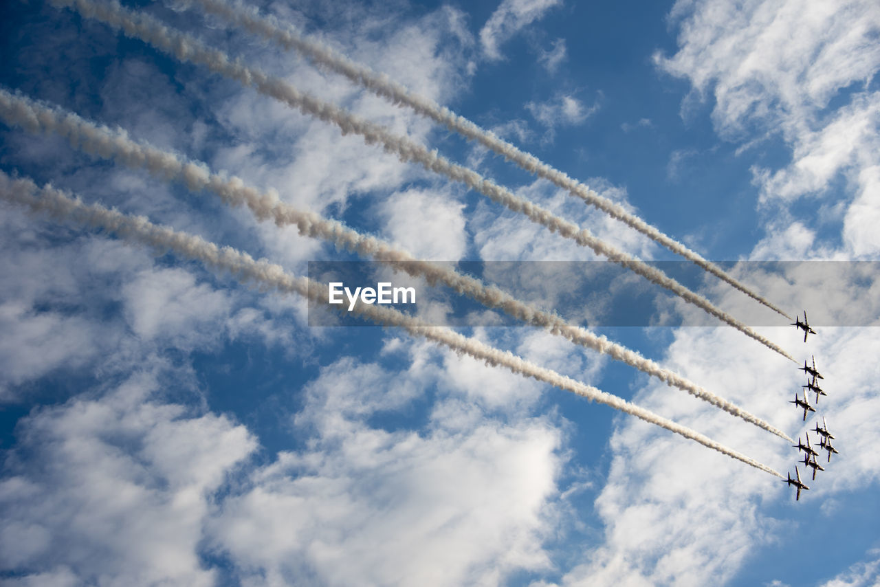 Low angle view of airplane emitting vapor trail against blue sky
