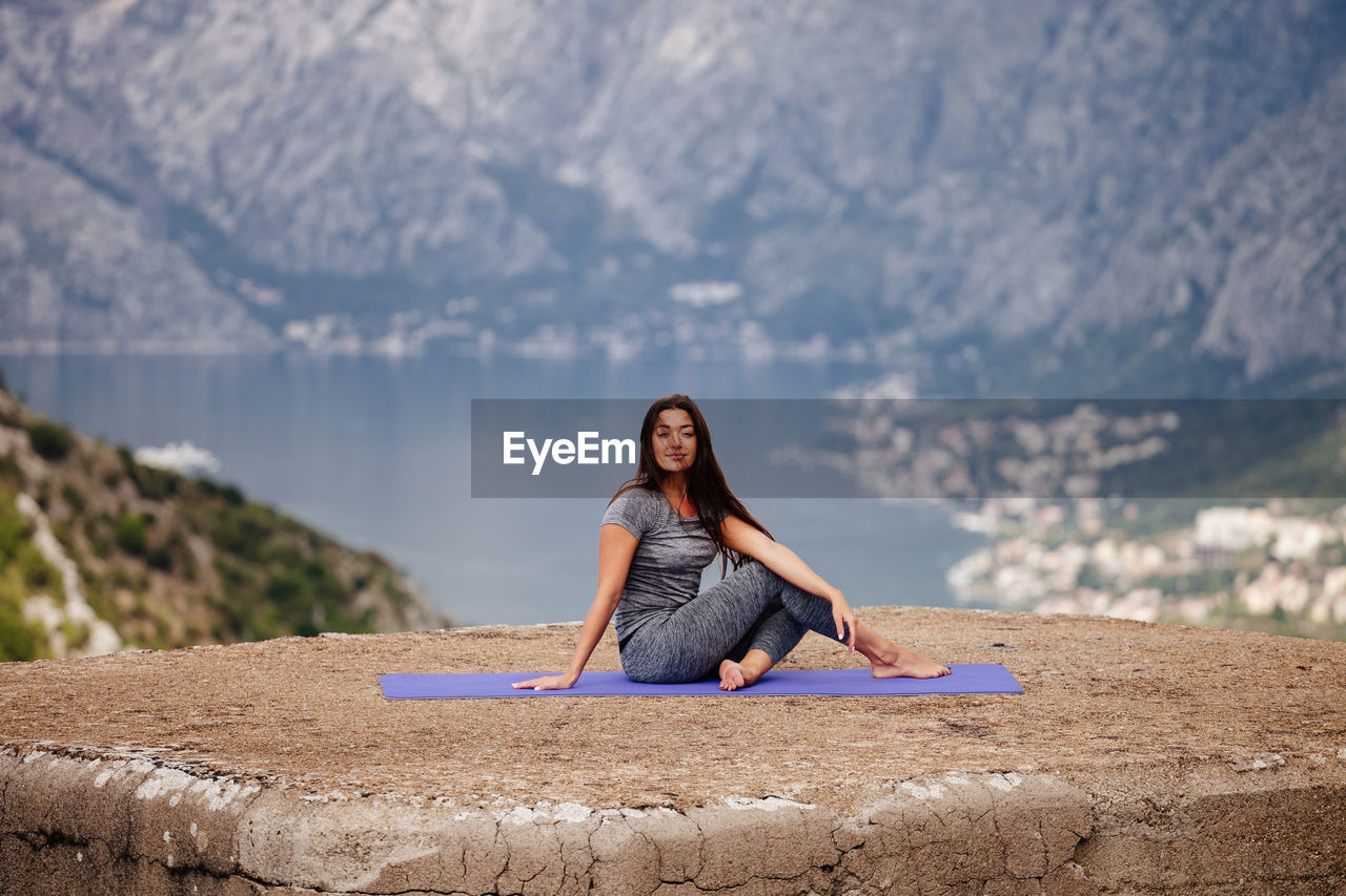 Portrait of young woman exercising on cliff against mountain