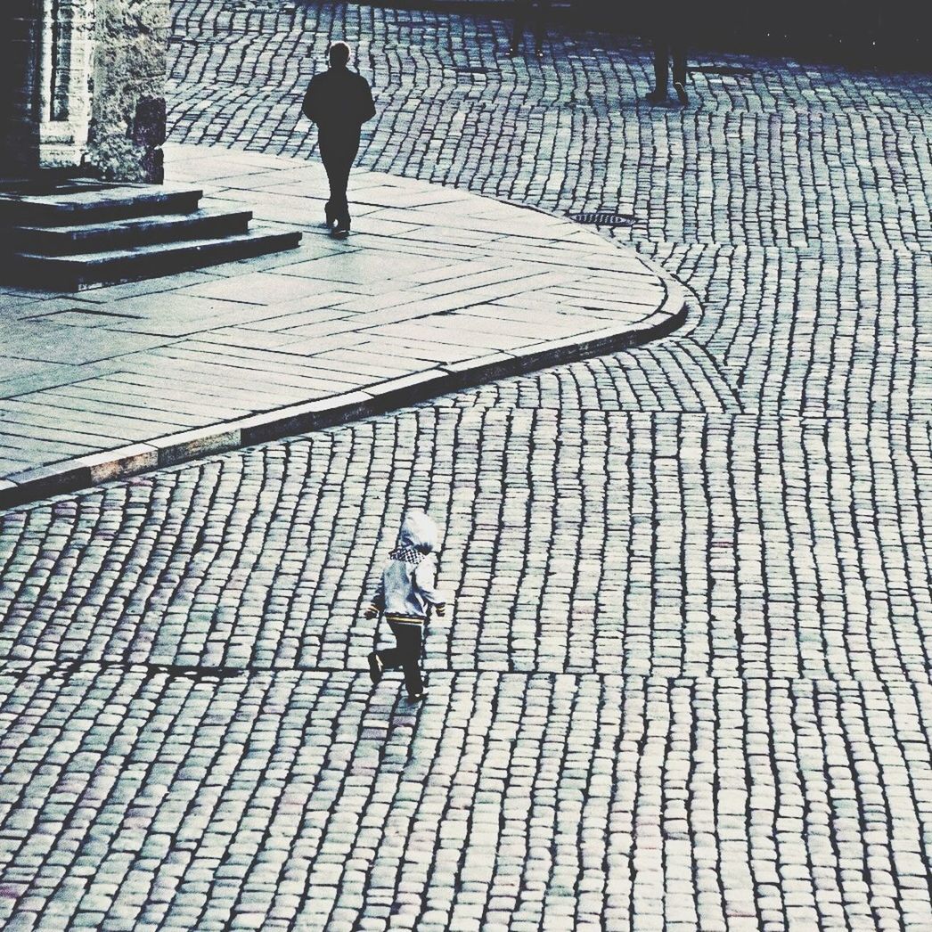 High angle view of child running on paving stones while man walking on sidewalk