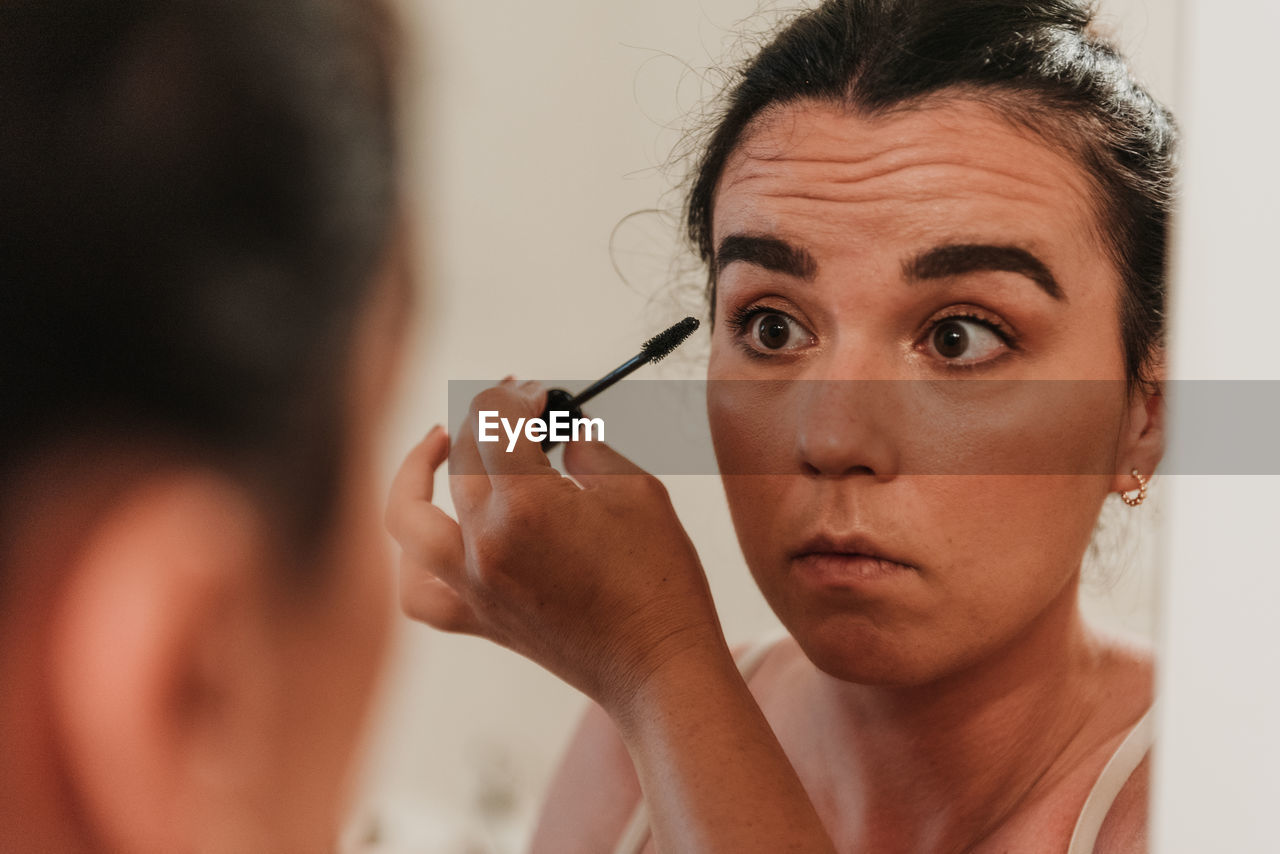 Mirror photo of beautiful young woman putting on makeup