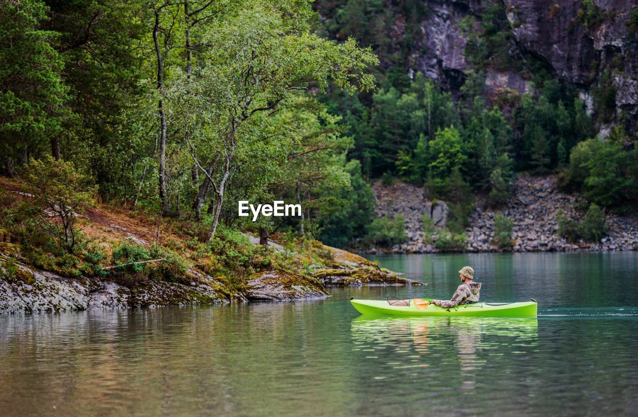 Side view of man sailing boat in lake against trees