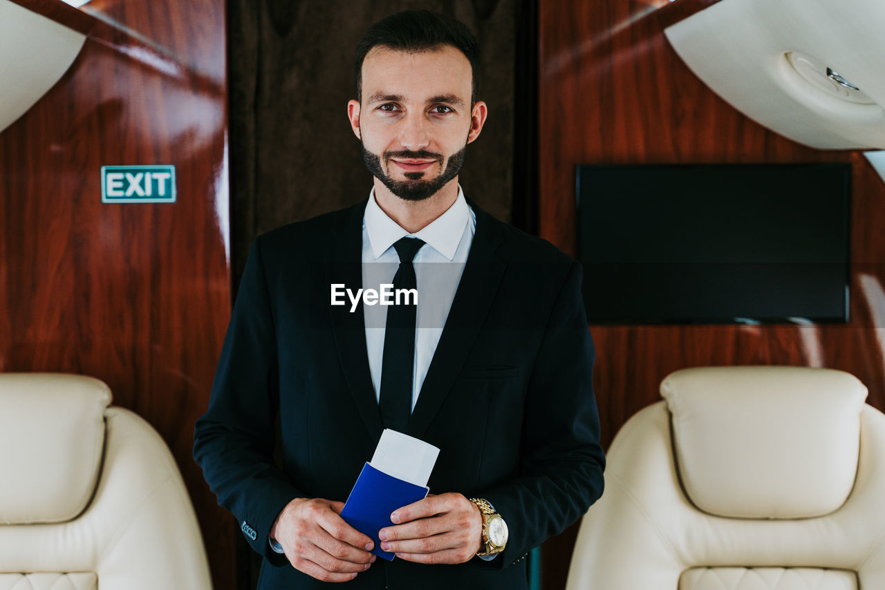 PORTRAIT OF A SMILING YOUNG MAN HOLDING CAMERA IN A ROOM