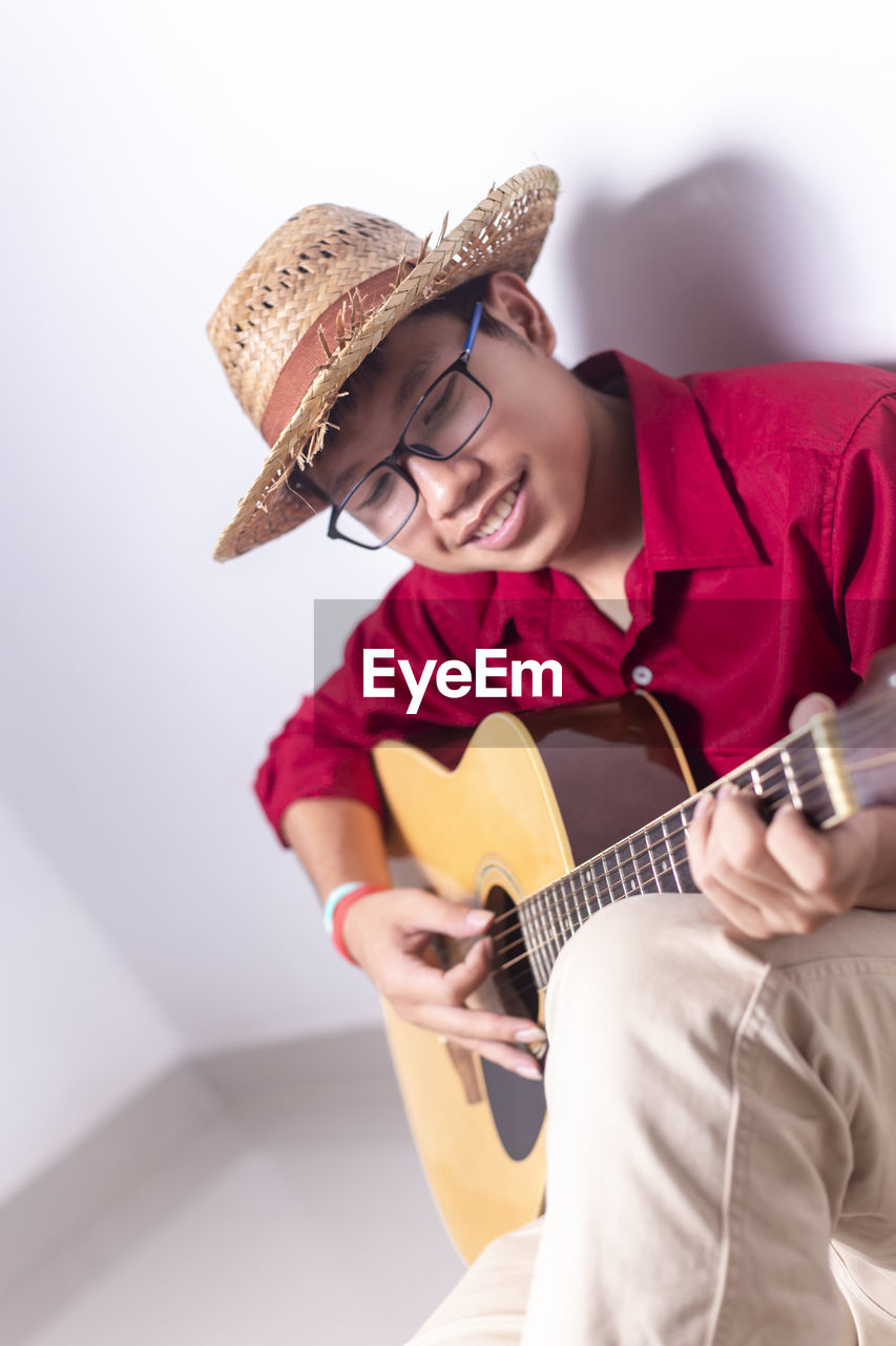 Man playing guitar while sitting against wall