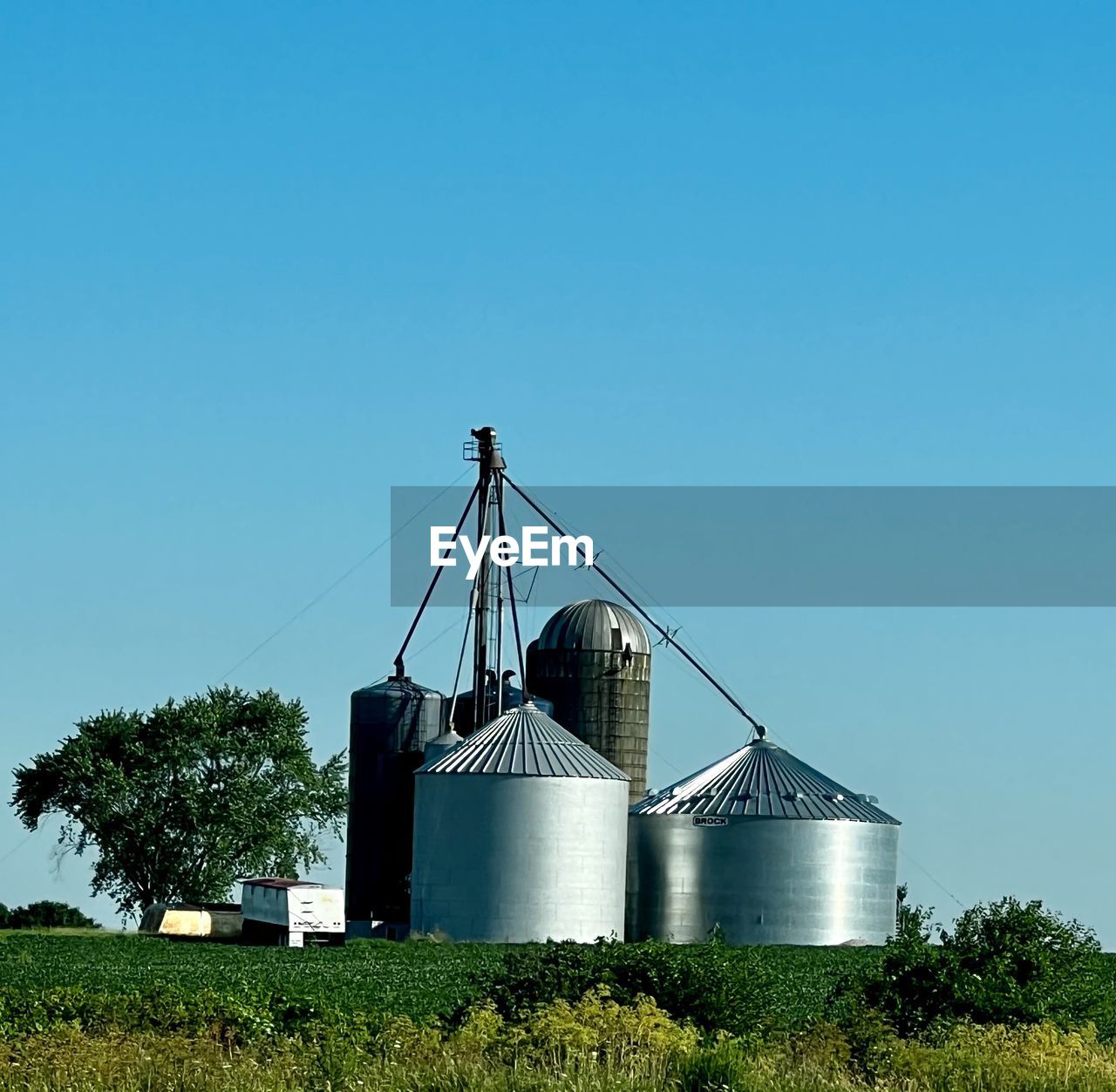 sky, silo, architecture, built structure, plant, nature, blue, tower, agriculture, no people, clear sky, industry, building, copy space, building exterior, landscape, rural scene, day, farm, factory, windmill, storage tank, outdoors, environment, metal, power generation, rural area, sunny, tree, land, mill