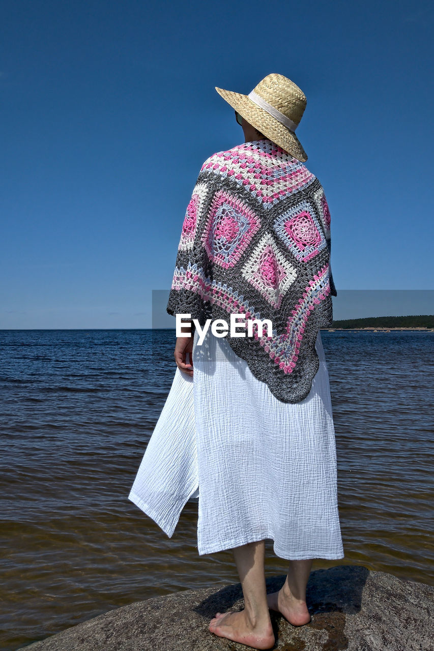 Rear view of woman with hat on beach against clear sky