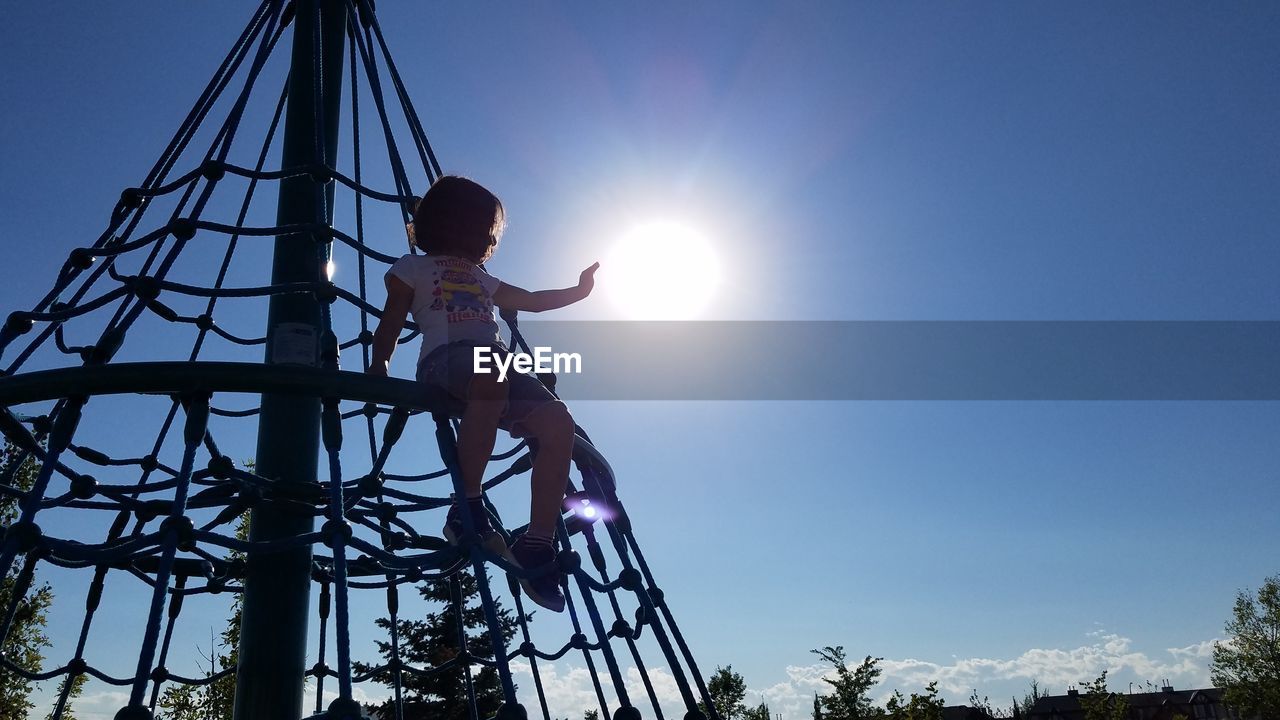 Low angle view of girl sitting on play equipment against clear sky