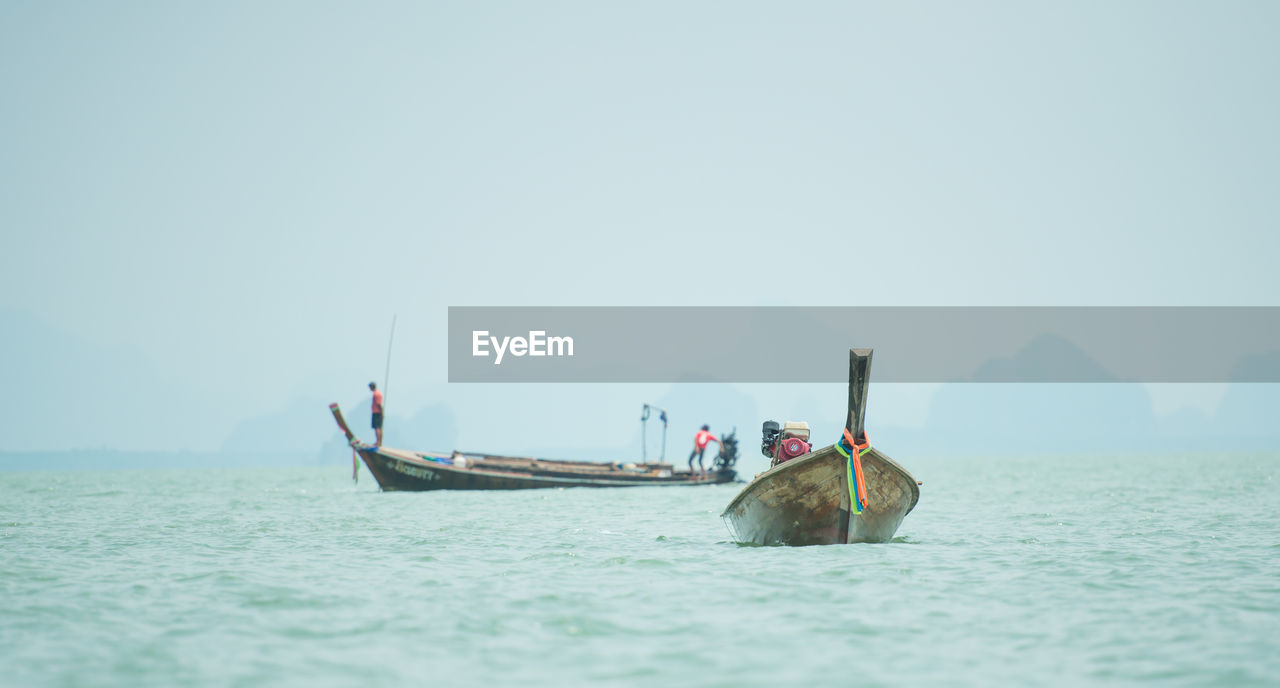 PEOPLE FISHING IN SEA AGAINST SKY