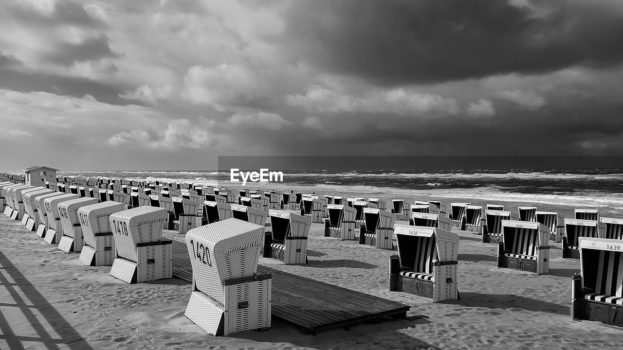 HOODED BEACH CHAIRS ON SAND AGAINST SKY