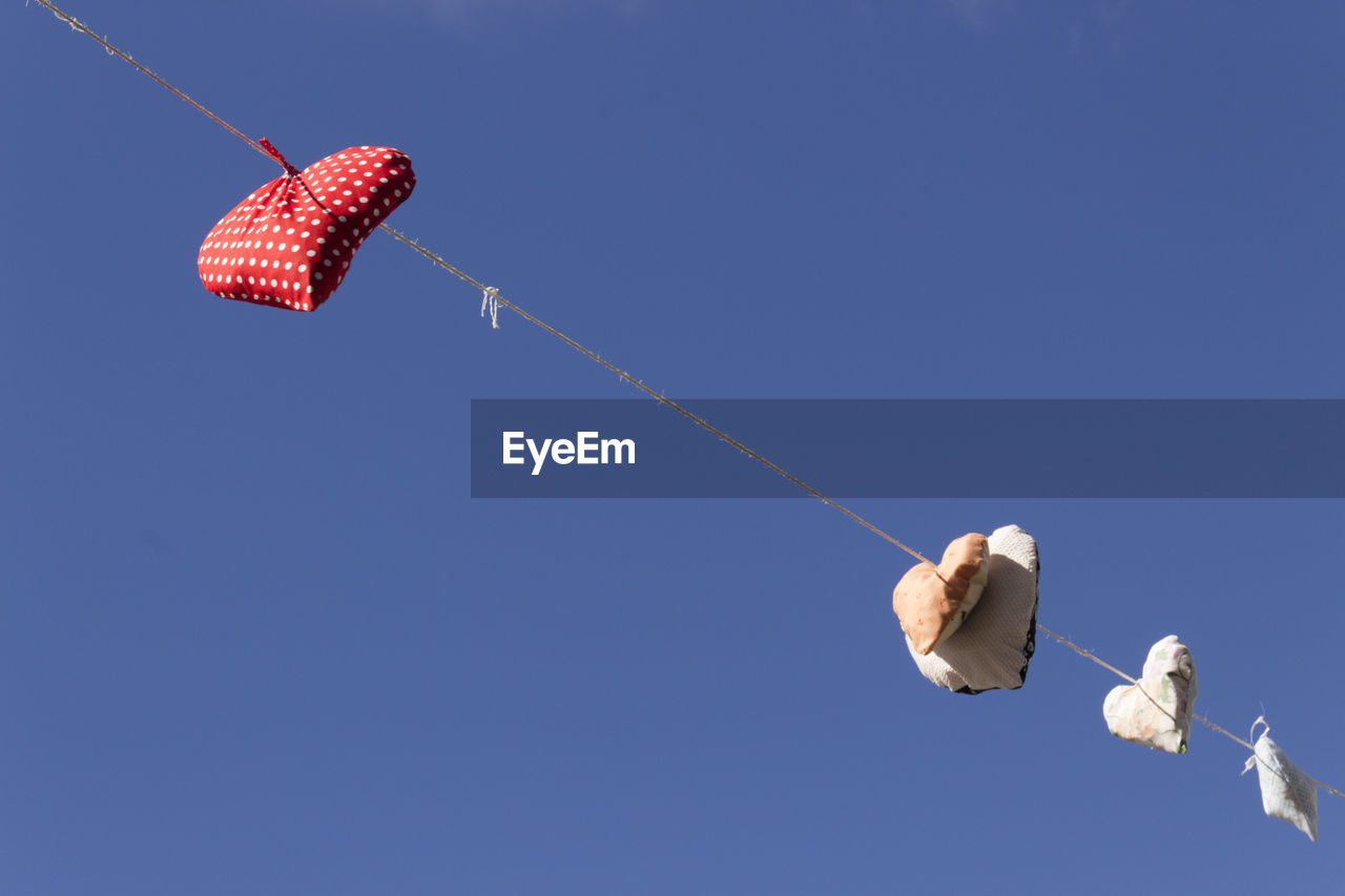 Low angle view of heart shape cushions hanging on rope against clear blue sky