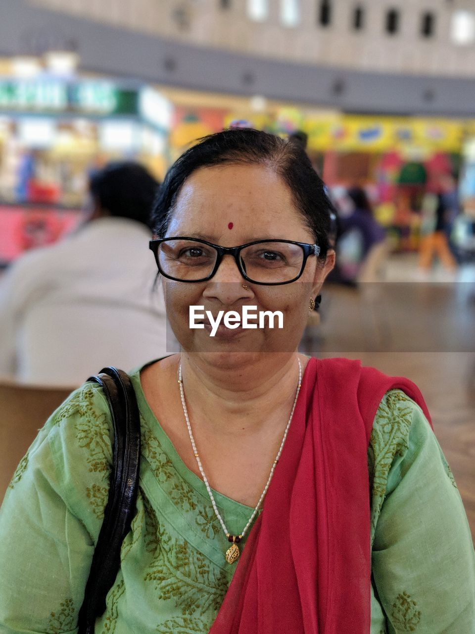 Portrait of smiling mature woman wearing eyeglasses while sitting indoors