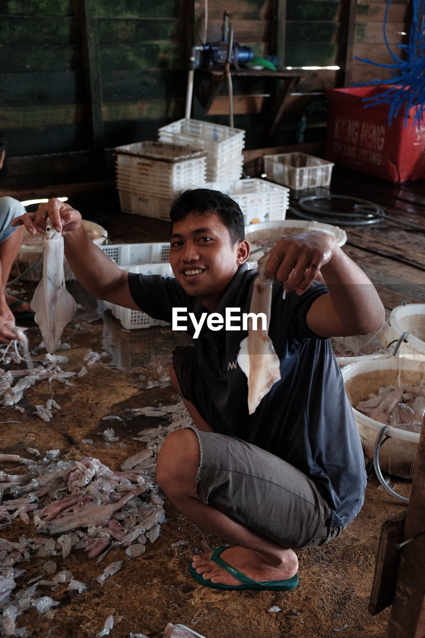 Portrait of smiling man holding cuttlefish fishes while crouching at fish market