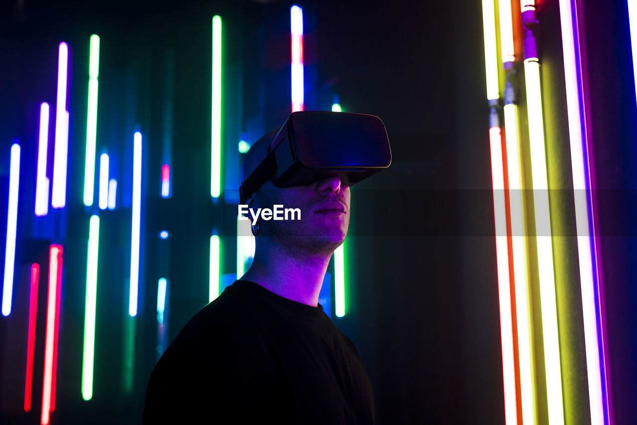 Man wearing vr glasses near multi colored illuminated lights