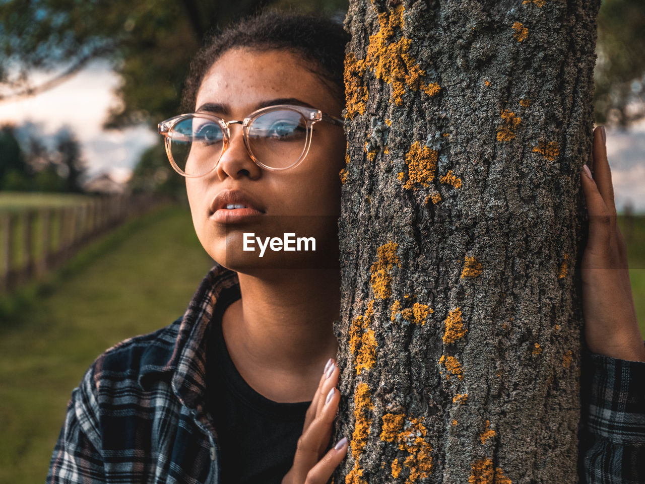 Close-up of young woman standing by tree trunk