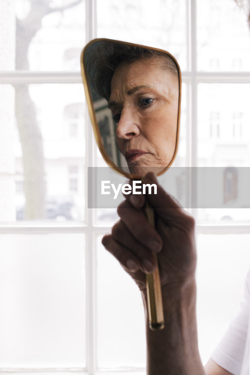 Reflection of worried senior woman in mirror at home