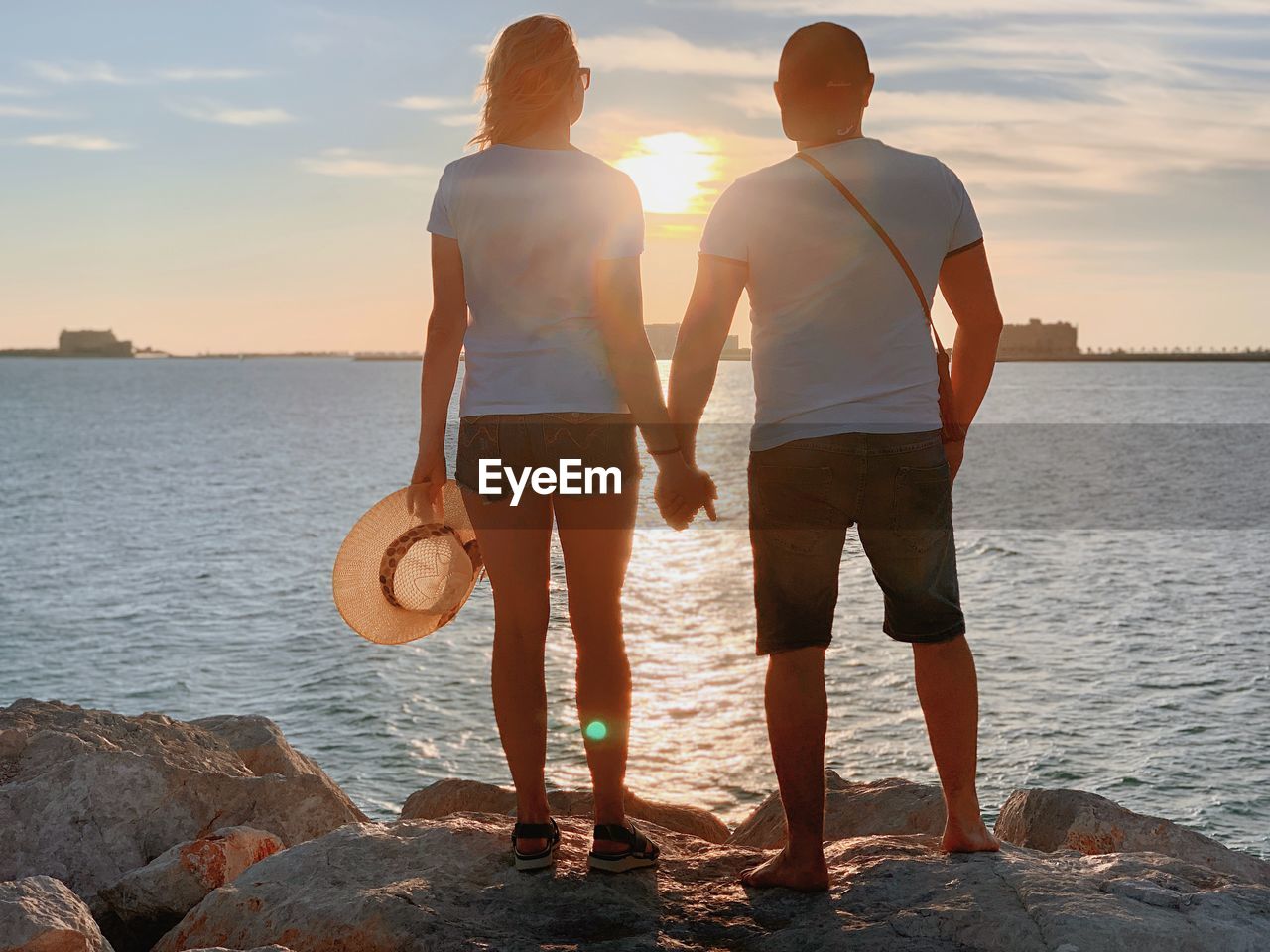 REAR VIEW OF MEN STANDING AT BEACH AGAINST SKY