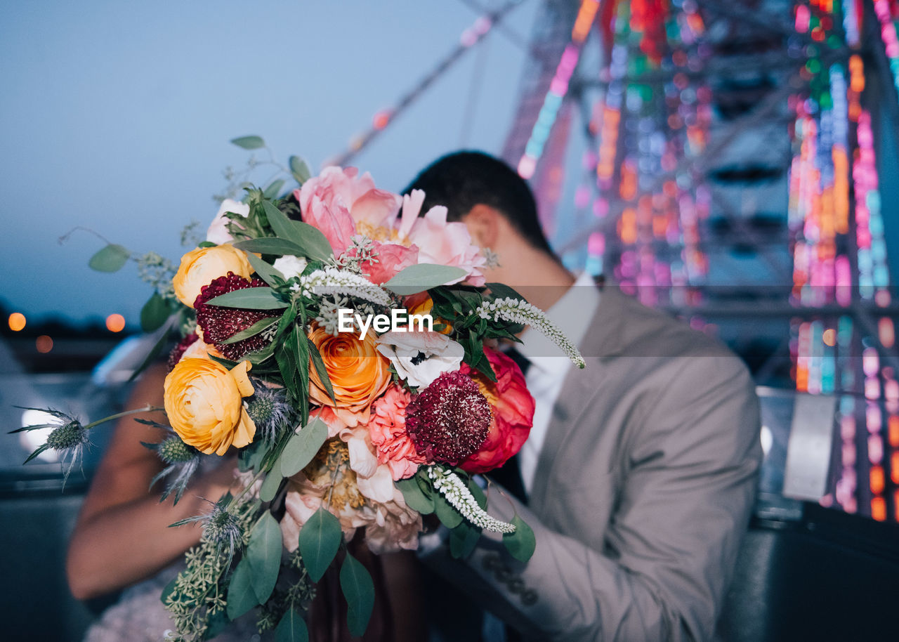 Couple covering face with flower bouquet during wedding ceremony