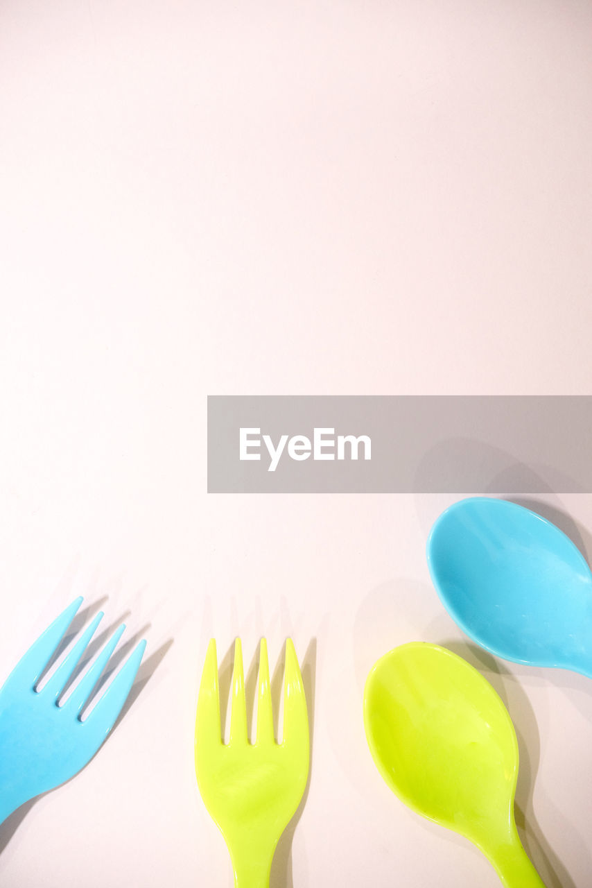 Close-up of disposable plastic forks and spoons on colored background