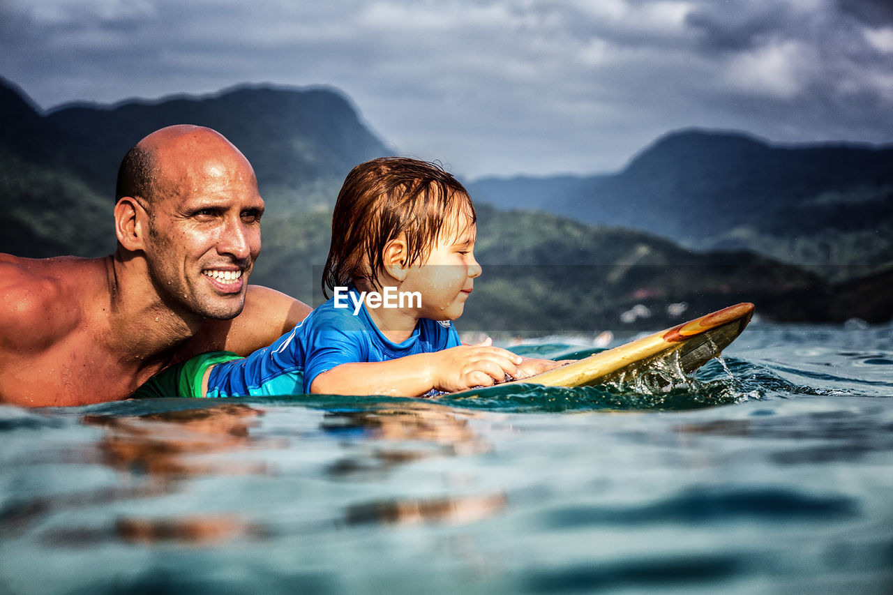 Father and 3 year old sun paddling on a wooden surfboard