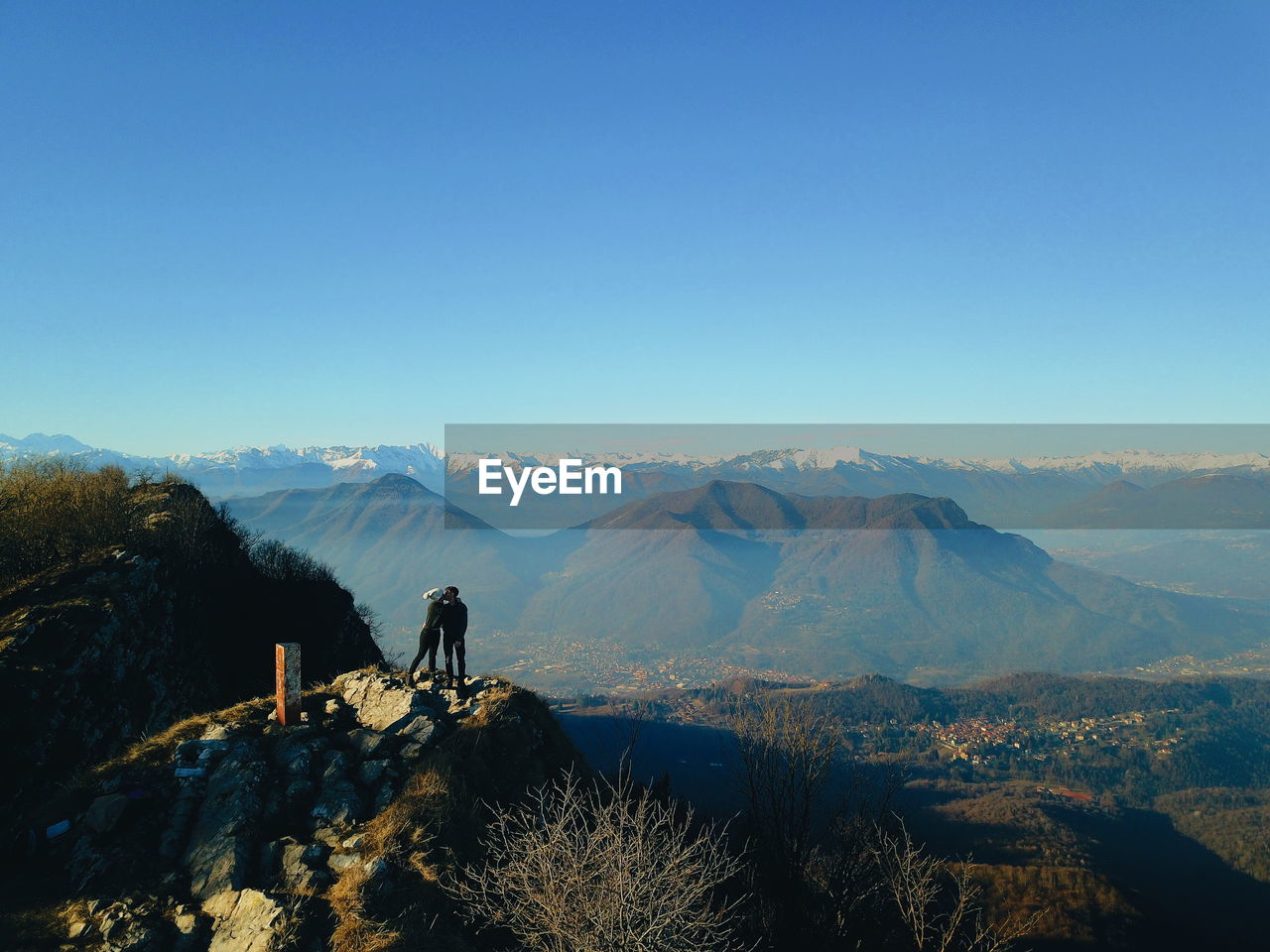 Side view of young couple kissing while standing on mountain against sky