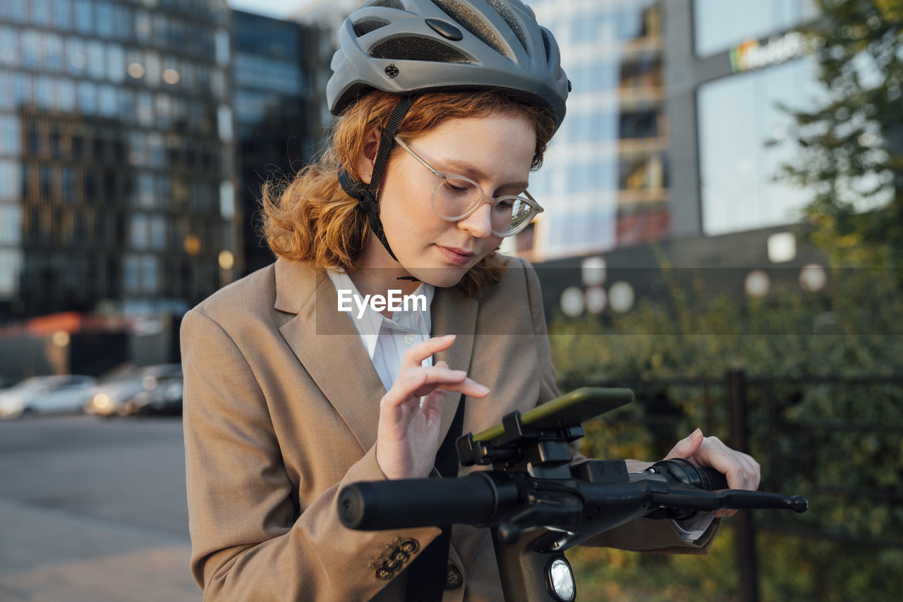 Young businesswoman using smart phone on electric push scooter