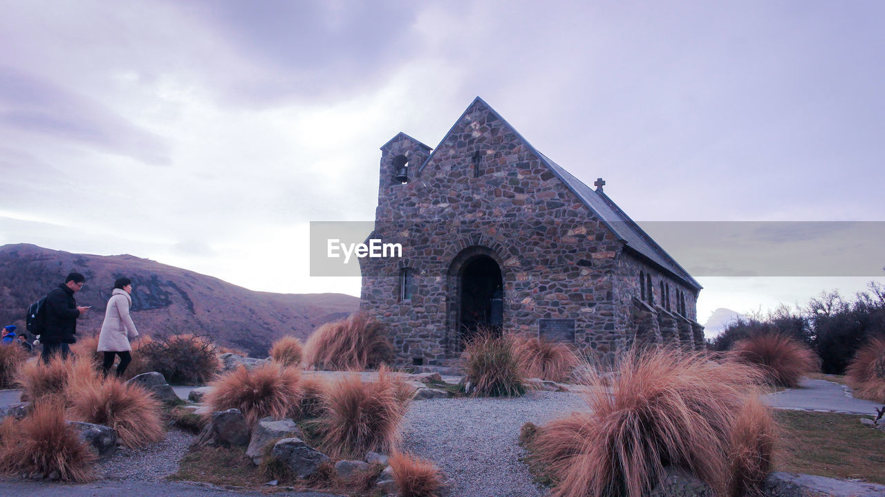 People walking towards old church against sky at sunset