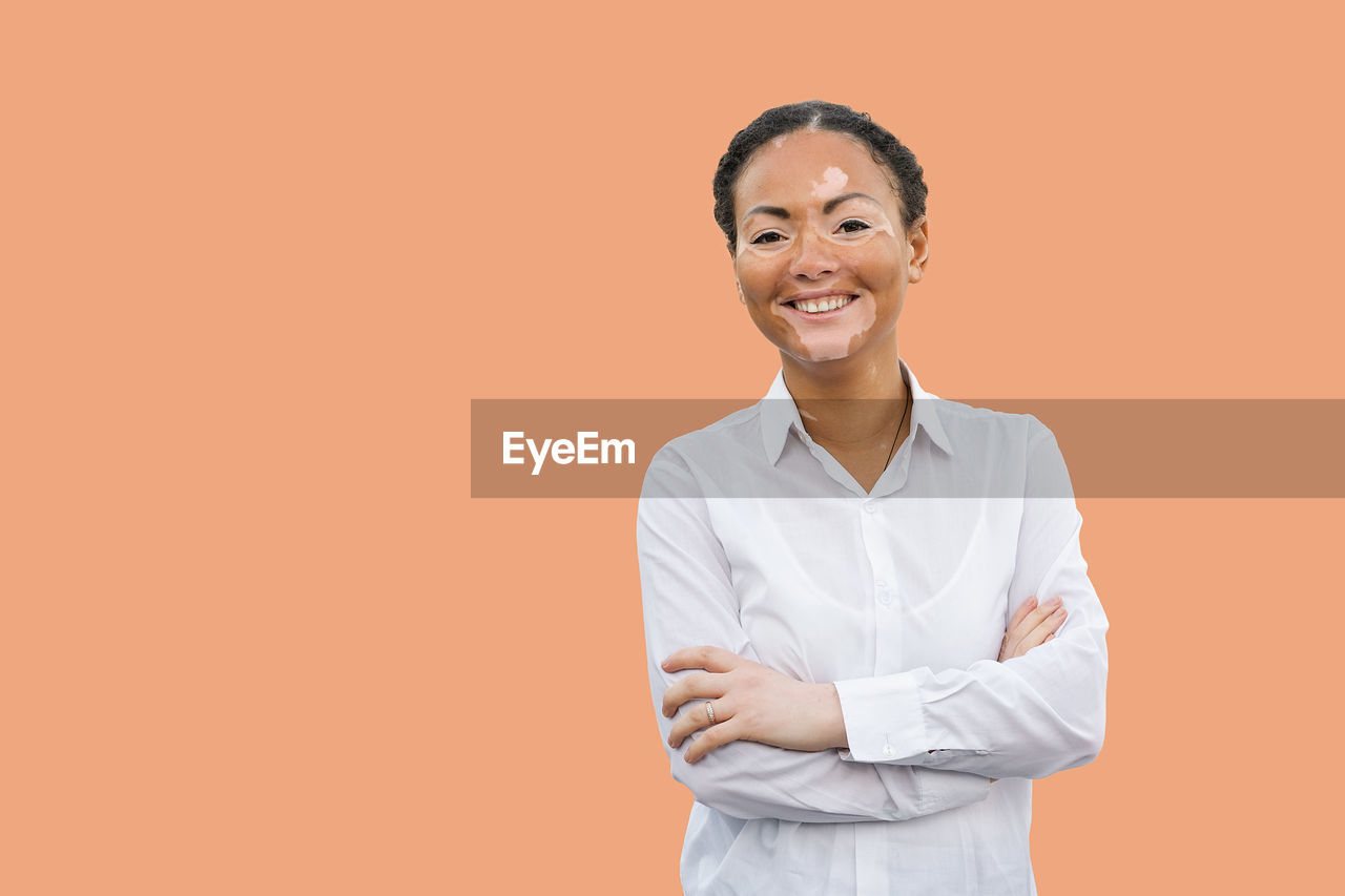 Portrait of young woman suffering from dermatitis standing against orange background