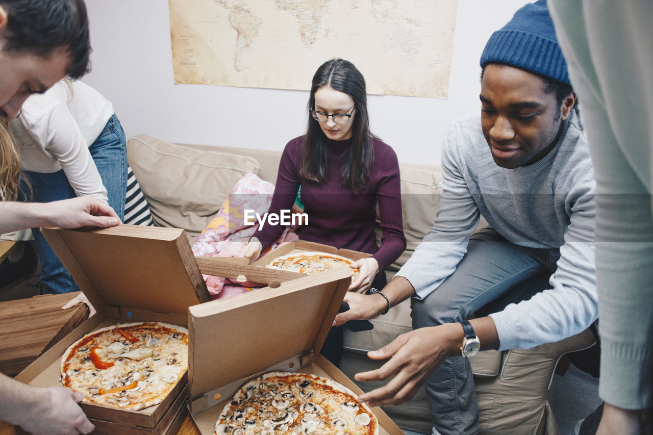 High angle view of young friends opening pizza boxes in dorm room