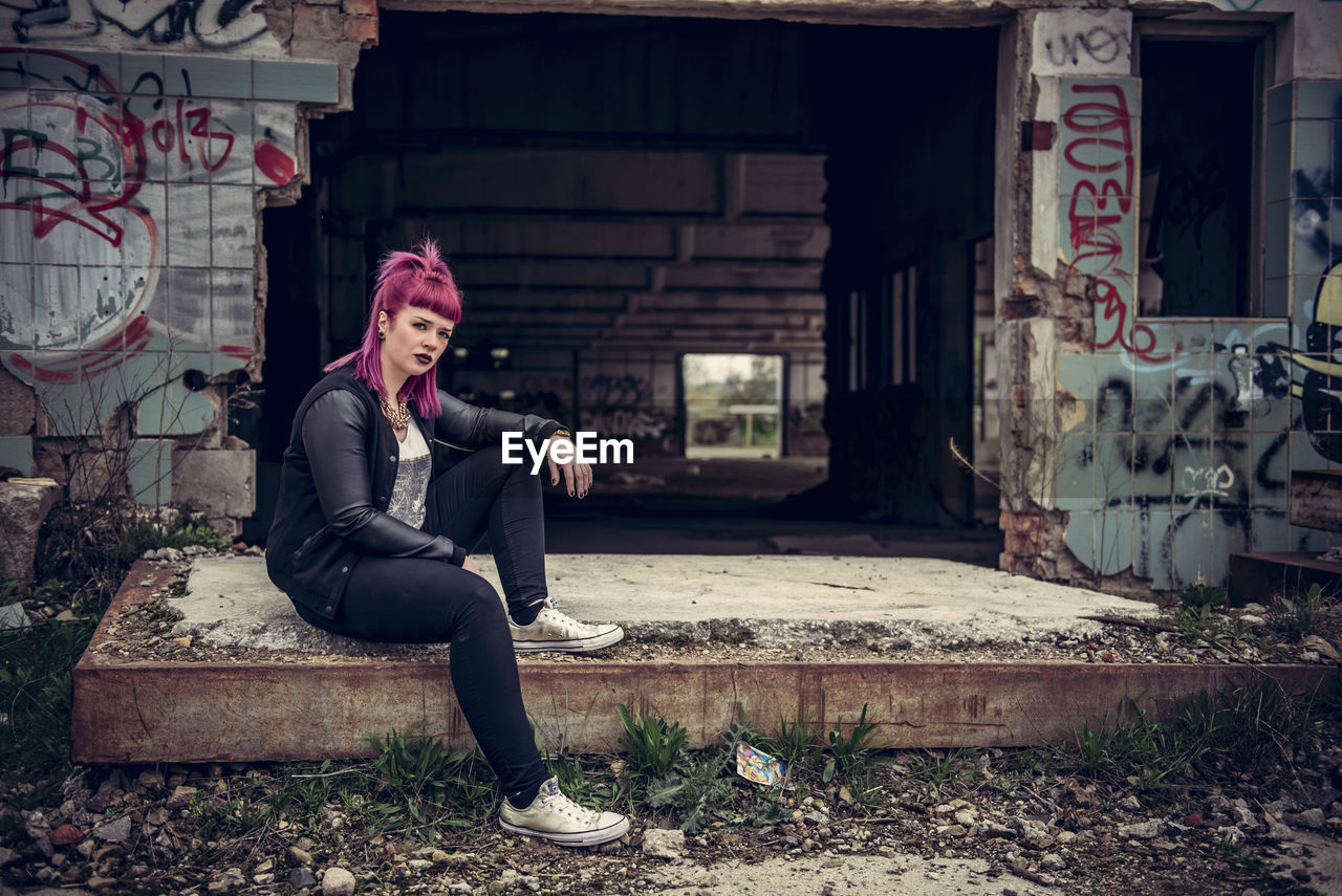 Portrait of young woman sitting by abandoned building