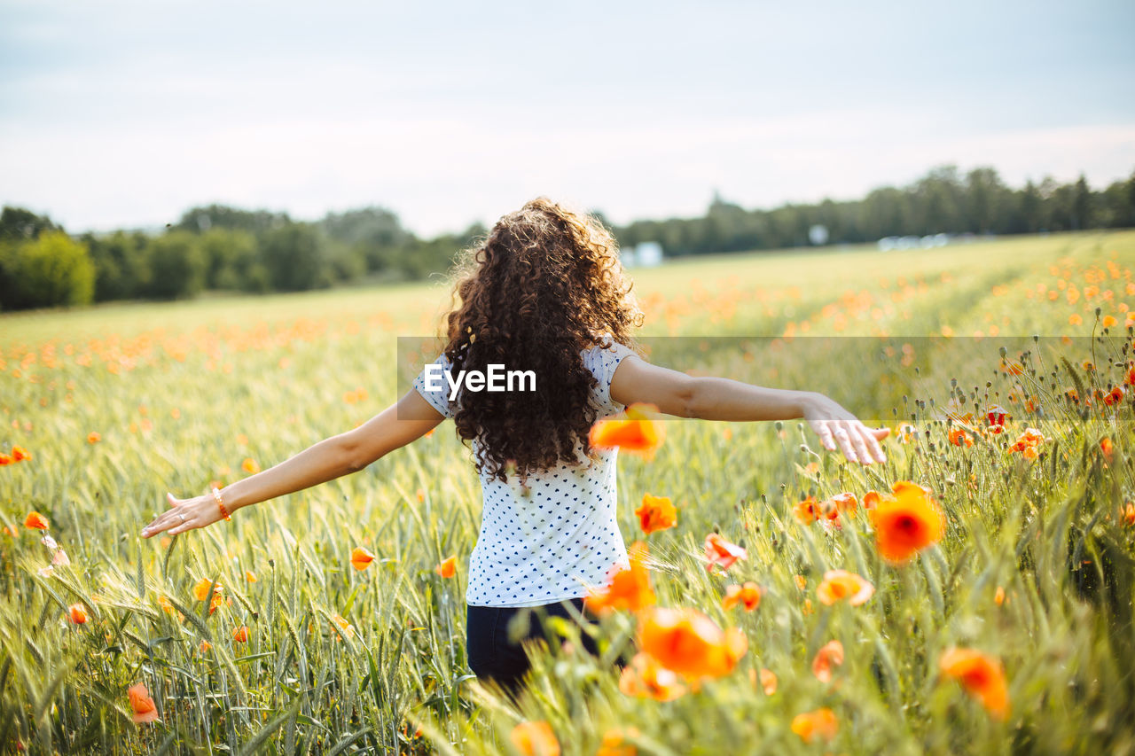 Woman with arms outstretched standing on field against sky