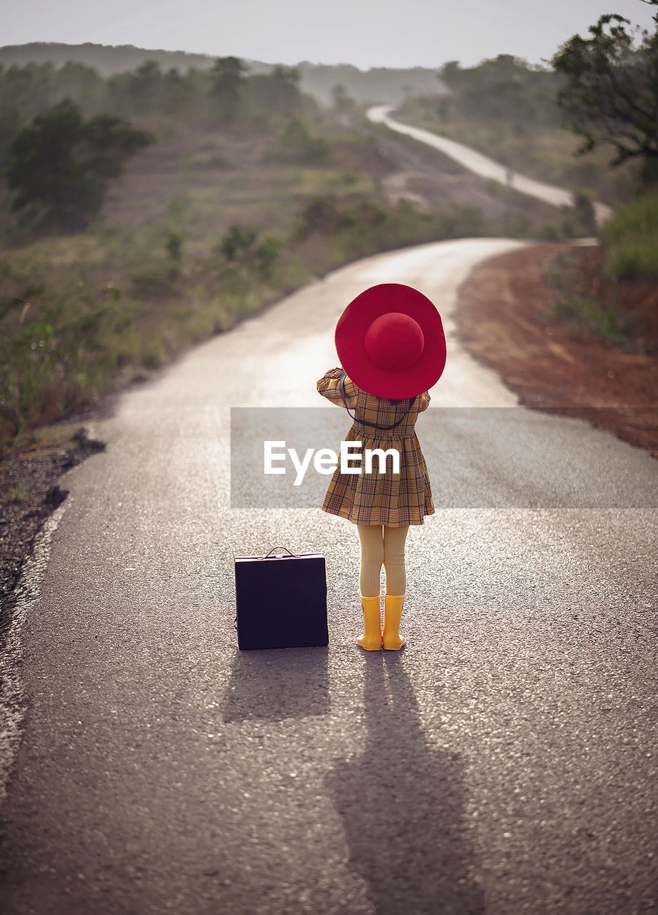 Rear view of girl with suitcase standing on road