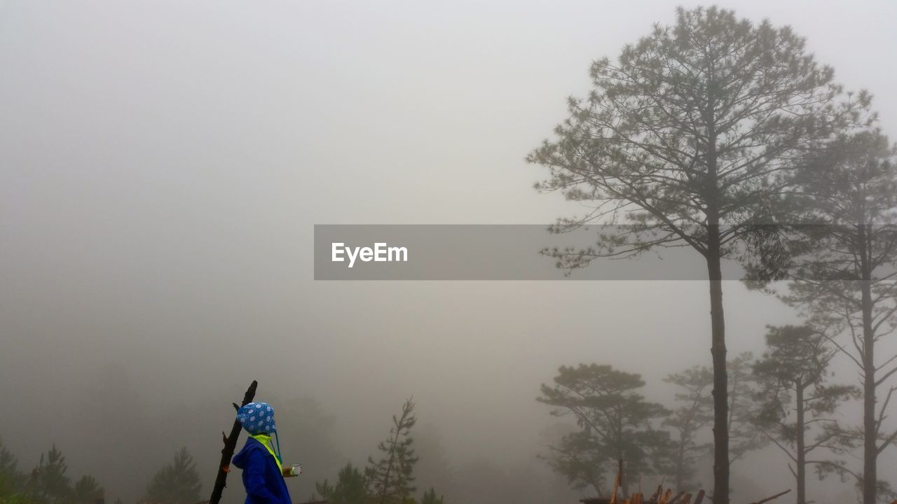 REAR VIEW OF MAN STANDING IN FOGGY WEATHER