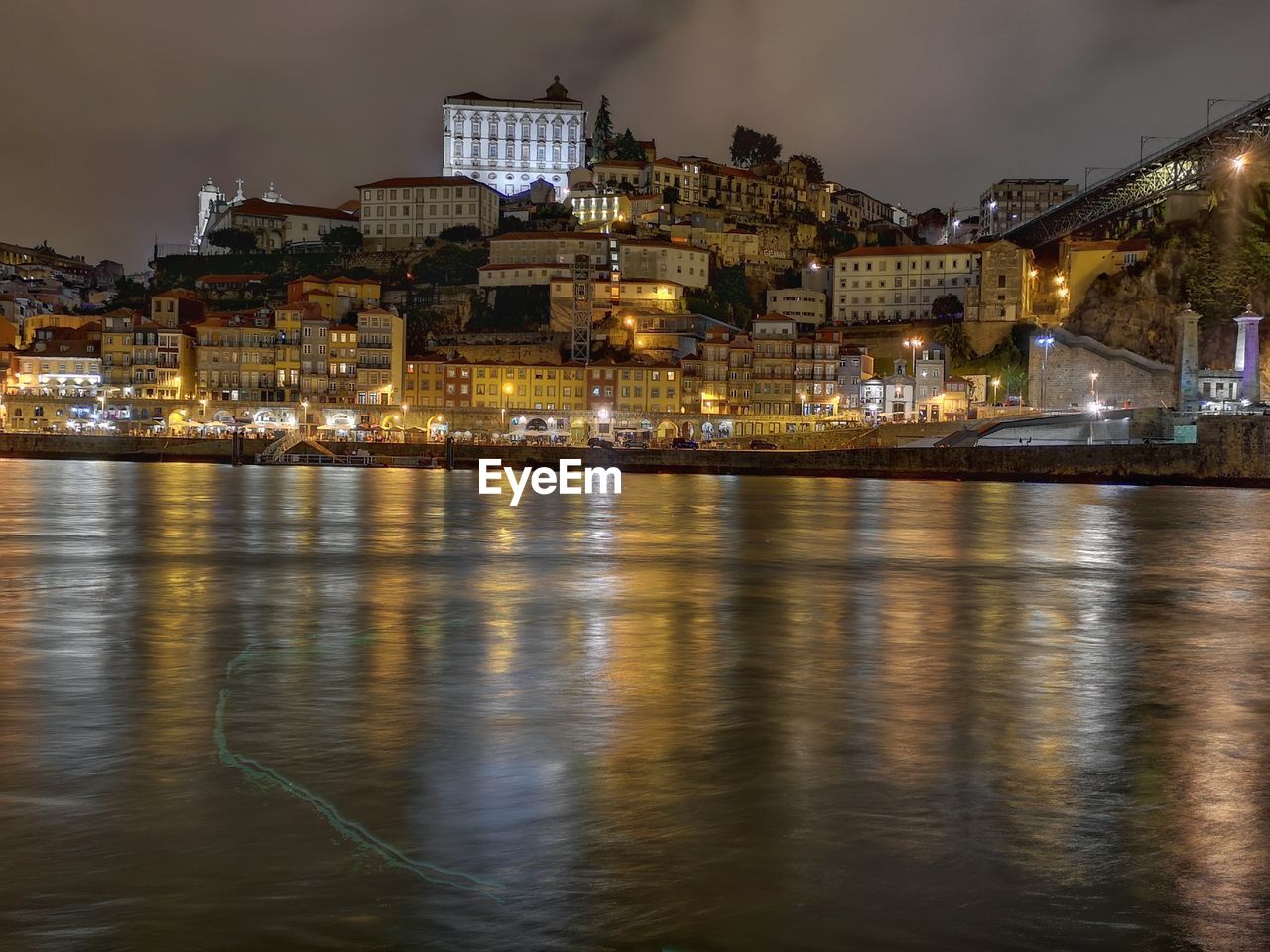 Illuminated buildings by river against sky at night