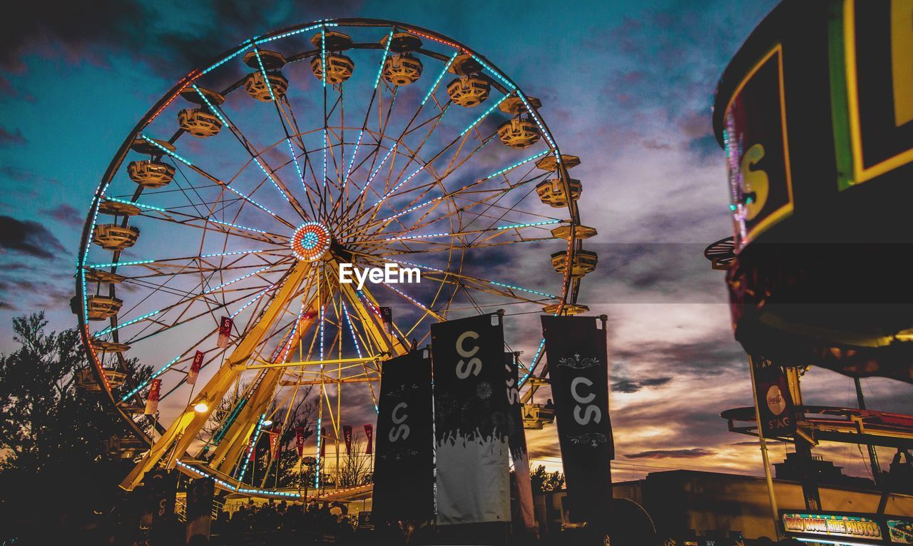 LOW ANGLE VIEW OF ILLUMINATED FERRIS WHEEL AGAINST SKY AT DUSK